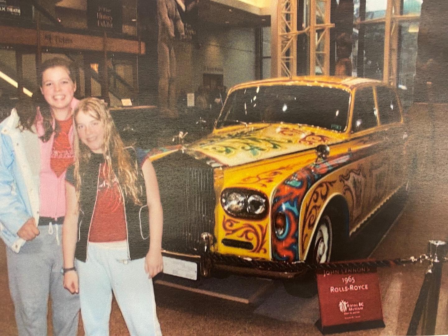 Two sisters, standing in front of a car at the museum.