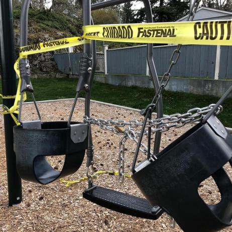 Playground swings wrapped in yellow "caution" tape.
